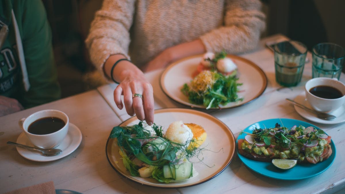 Crop anonymous female eating healthy meal served on plate with coffee on table in restaurant